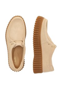 Beige Wildlederschuhe mit runder Zehenform, Schnürdesign und einer dicken braunen Gummisohle mit horizontalen Rillen.