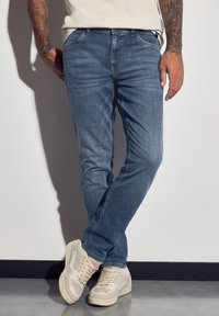 Jasnoniebieskie dżinsy o luźnym kroju, z klasycznym pięciopocketowym designem i subtelnym wyblaknięciem, zestawione z beżowymi trampkami.