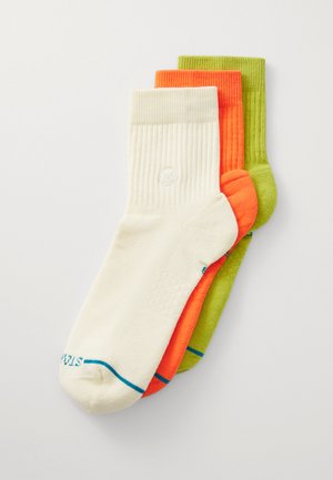 Three pairs of socks in cream, orange, and green. Features ribbed design, soft texture, and tonal stitching with logo detail on cream sock.