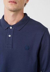 Polo shirt blu navy in cotone. Presenta un colletto classico, una patta con tre bottoni e un tessuto testurizzato. Include un logo in rilievo.