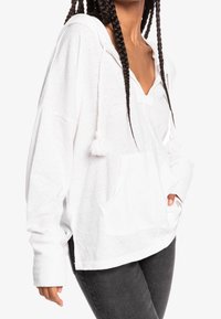 Biała hoodie z dekoltem w serek, kieszenią z przodu i sznurkami zakończonymi frędzlami. Wykonana z miękkiego materiału, z długimi rękawami i luźnym krojem.