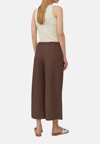 Pantalons amples marron avec un tissu texturé et un waistband élastique, associés à un top sans manches crème et des sandales de couleur claire.