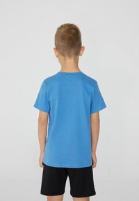 Blaues Baumwoll-T-Shirt mit kurzen Ärmeln und Rundhalsausschnitt, von hinten präsentiert. Kombiniert mit schwarzen Shorts, die ein einfaches Design zeigen.
