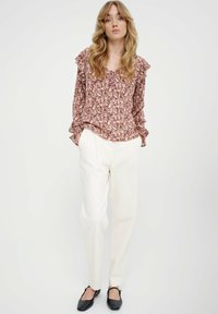 Kwiatowa bluzka z falbaniastymi rękawami, w odcieniach r�óżu, bieli i zieleni; zestawiona z kremowymi spodniami w taperze i czarnymi balerinkami.