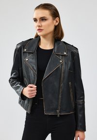 Giacca da biker nera in pelle con hardware in argento, tasche con zip e colletto a scollo a V con cuciture a contrasto.