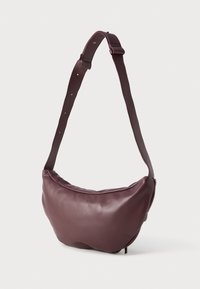 Sac à épaule en cuir brun au design courbé, avec une large sangle et une texture lisse. Il dispose d'une fermeture éclair et d'un design minimaliste.