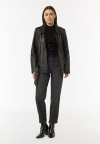 Schwarze Lederjacke mit Reißverschluss, gestreifter schwarzer Pullover mit Pailletten, graue hochtaillierte Jeans und schwarze Absatzstiefeletten.