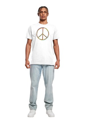 Hvid bomulds t-shirt med et stort, farverigt fredssymbol-tryk på forsiden. Modellen har lyseblå jeans og hvide sneakers på.