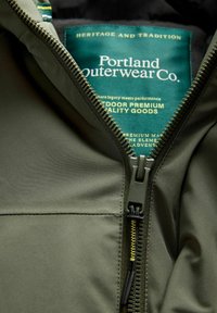 Zelena zunanja jakna z zadrgo na sprednji strani, ki ima gladko teksturo in oznako "Portland Outerwear Co" znotraj.