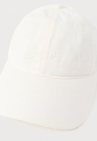 Gorra blanca de algodón con visera curvada. Presenta un texto bordado que dice "Boys" en estilo cursivo. Tejido texturizado con detalles de costuras visibles.