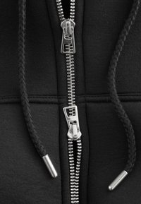 Schwarzer Hoodie mit metallischem Reißverschluss und geflochtenen Kordeln. Verfügt über glattes Gewebe und silberne Beschläge.