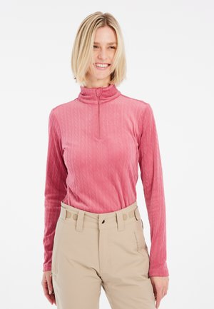 Maglia a maniche lunghe color rosa polveroso con colletto alto, motivo a treccia testurizzato e zipper a metà. Abbinata a pantaloni beige chiaro.