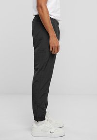 Pantaloni jogger negri, con croieli taper, talie elastică, buzunare laterale și manșete ribbate, asortați cu pantofi sport albi cu accente din plasă.