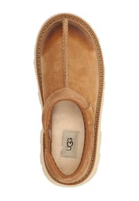 Scarpa slip-on in suede marrone con morbida fodera interna, dettagli cuciti e una spessa suola in gomma beige. Logo UGG visibile sulla soletta.