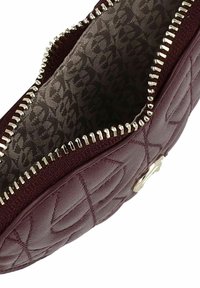 Pochette en cuir matelassé bordeaux avec une fermeture éclair lisse, une doublure en tissu à motifs et un petit accent métallique à l'extérieur.