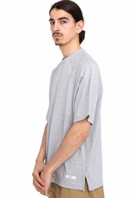 Šedé oversized tričko z měkkého bavlněného materiálu s krátkými raglánovými rukávy, kulatým výstřihem, bočními rozparky a malou nášivkou na lemu.