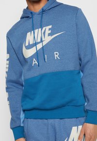 Blå hoodie med ljusa och mörka blå segment, med stor vit Nike Air-logga på framsidan och ärmen. Dragkedja i huvan och mjukt material.