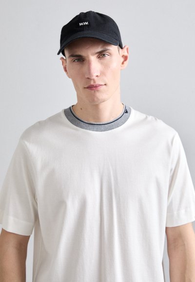 Balta medvilninė marškinėliai su apvaliu pilku ir tamsiai mėlynu apykakle, derinami su juoda kepure, kurios priekyje užrašyta balta„W.W.“.