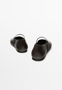 Brown leather flats with a rounded shape, featuring a low back and a thin strap across the ankle. Smooth texture and minimalistic design.