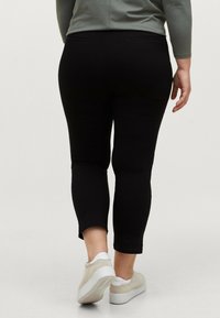 Sorte leggings med en glat tekstur, cropped længde og diskrete baglommer, parret med lyse, runde sneakers.