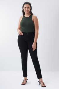 Jeans negros de cintura alta con diseño ajustado, combinados con un bodysuit sin mangas de color verde oscuro. Llevado con sandalias negras de tacón y hardware mínimo.