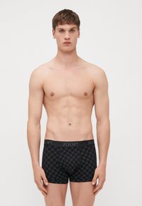 Fekete boxeralsó geometrikus mintázattal és szürke derékszíjjal, amelyen a "JOOP!" márkaneve félkövér betűkkel szerepel. Sima anyagú textúra.