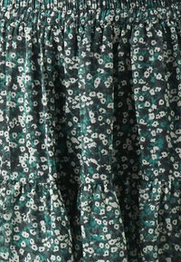 Virágmintás textil sötétzöld és fehér árnyalatokban, fodros, texturált dizájnnal, réteges szegéllyel.