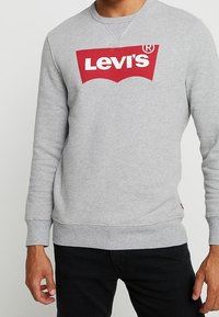 Sudadera gris de algodón con cuello redondo, que presenta un gran logo de Levi's en rojo en el frente y puños y dobladillo acanalados.