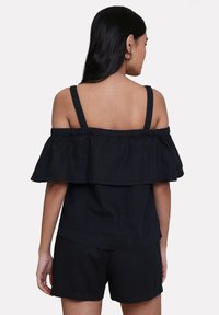 Top nero off-the-shoulder con un design a strati di volant, spalline regolabili e una vestibilità rilassata, abbinato a pantaloni corti neri coordinati.