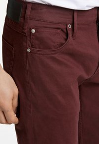 Bordeaux denim jeans met een voorzak, zilveren klinknagels en een lederen label op de tailleband, met een gladde textuur en een klassieke pasvorm.