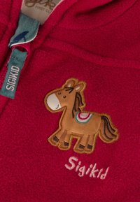 Rotes Fleece-Kleidungsstück mit einem braunen gestickten Pferdemotiv und bunten Satteldetails. Das Markenetikett trägt die Aufschrift "Sigikid."