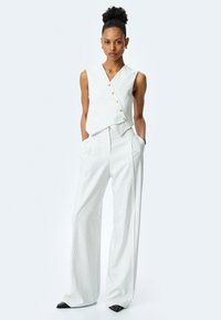 Top sin mangas de rayas blancas con diseño cruzado y botones dorados, combinado con pantalones anchos de rayas que cuentan con bolsillos laterales y una textura suave.