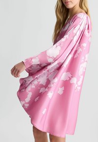 Vestito floreale rosa con maniche lunghe, realizzato in un tessuto morbido. Presenta un design largo e fluido con grandi motivi floreali bianchi in tutto il capo.
