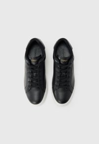 Mustadest nahast Coachi tossud mustade paelte ja valgete talladega, vaadatuna ülevalt valgel taustal.