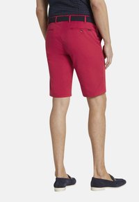 Rode katoenen shorts met een rechte snit, achterzakken en een zwarte geweven riem. Gecombineerd met marineblauwe instap schoenen.