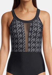 Maillot de bain une pièce avec un motif géométrique noir et gris, présenté avec un panneau transparent à l'avant et un bas noir uni.