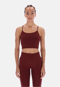 Bordowy zestaw odzieży sportowej składający się z crop topu z falbaniastym dołem oraz legginsów z wysokim stanem z teksturowanymi akcentami po bokach. Gładki, elastyczny materiał.