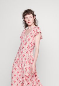 Vestido floral envolvente em rosa claro, com mangas curtas e volantes, decote em V e um detalhe de laço na cintura, apresentando uma saia fluida.