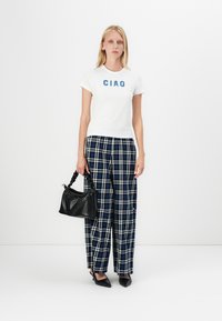 Hvit t-skjorte med blå "CIAO" tekst, kombinert med marineblå og hvite rutete vidbukser. Svart teksturert håndveske og spisse sko.