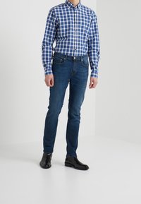 Camicia a maniche lunghe a quadri blu e bianchi, jeans blu scuro e stivaletti neri alla caviglia. Design slim fit, tessuto di cotone, texture liscia.