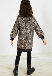 Abito a maglione oversize con stampa leopardata, maniche lunghe a palloncino, polsini e orlo a costine neri; abbinato a leggings neri e stivaletti.