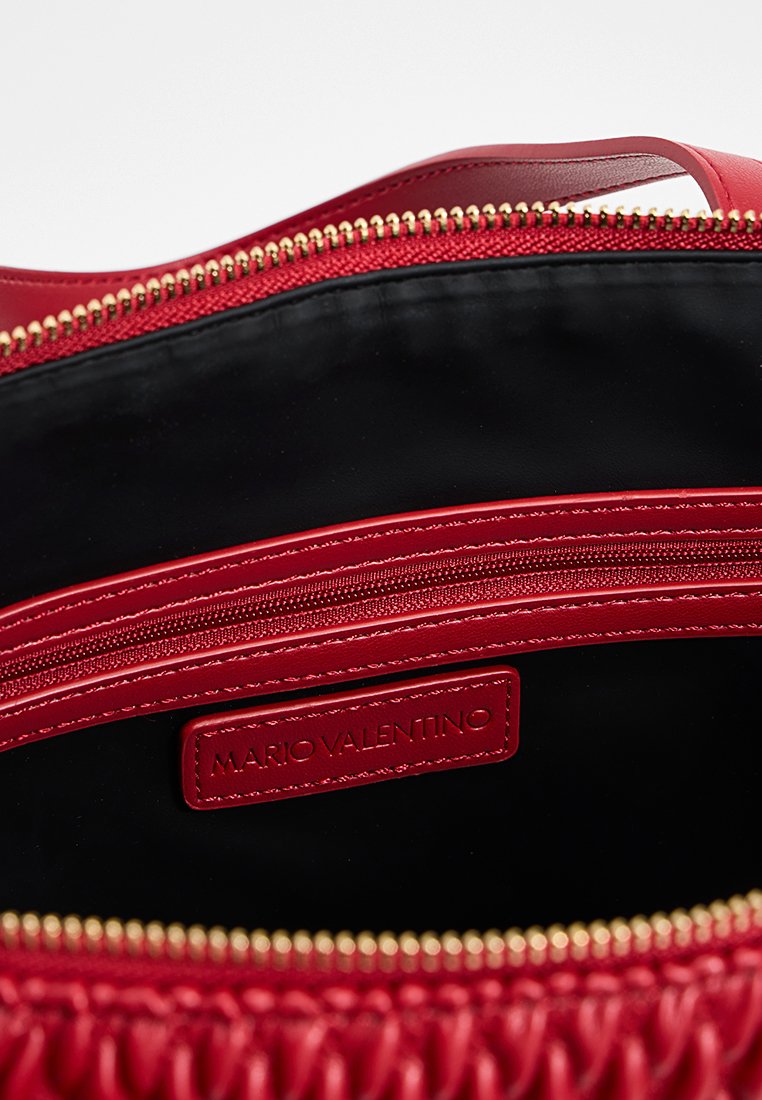 Intérieur d'un sac en cuir rouge avec une poche zippée et une étiquette de marque "MARIO VALENTINO" cousue à l'intérieur.