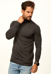 Dunkelgrauer Rollkragenpullover aus weichem Stoff, taillierte Passform, gerippte Bündchen und Saum, getragen mit hellblauen Jeans und einer Uhr.