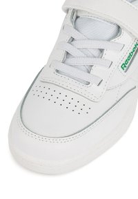 Białe trampki wykonane ze skóry, z perforacjami na palcach, sznurowane, z zielonym akcentem logo z boku.