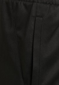 Pantaloni neri realizzati in un tessuto liscio e intrecciato con una leggera lucentezza, caratterizzati da un design frontale piatto e tasche laterali senza cuciture.