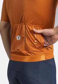 Oranje sportshirt met korte mouwen, voorzien van een achterzak en subtiele branding. Gekocht met donkerblauwe fietsbroek.