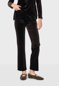 Čierne zamatové nohavice so štandardným strihom, v kombinácii s hnedými balerínami s zlatými štýlovými cvokmi. Mäkkučká textúra a elegantný silueta.