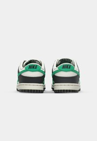 Αθλητικά παπούτσια Nike Dunk με γκρι και λευκό δερμάτινο επάνω μέρος, πράσινες λεπτομέρειες, υφή μαύρης καουτσούκ σόλας και έντονη σήμανση στη φτέρνα.