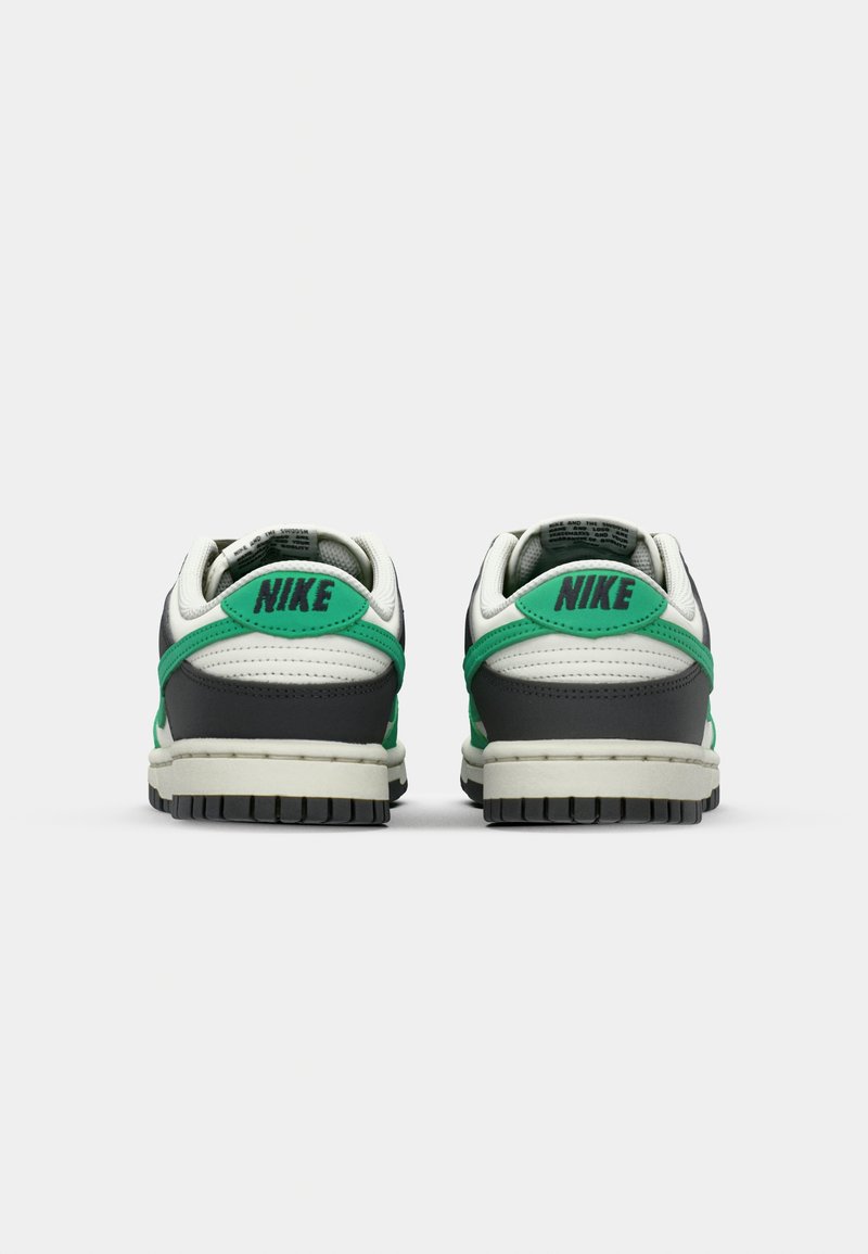 Baskets Nike Dunk avec une tige en cuir gris et blanc, des accents verts, une semelle en caoutchouc noir texturée et un marquage bien visible au niveau du talon.