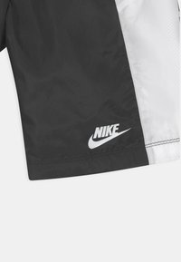 Pantalones cortos de Nike que presentan una combinación de paneles en blanco y negro, hechos de un tejido ligero, con un logo blanco visible en el dobladillo.